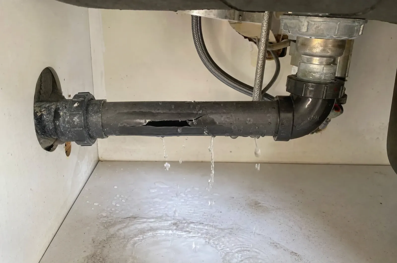 Split drain pipe leaking water under a kitchen sink